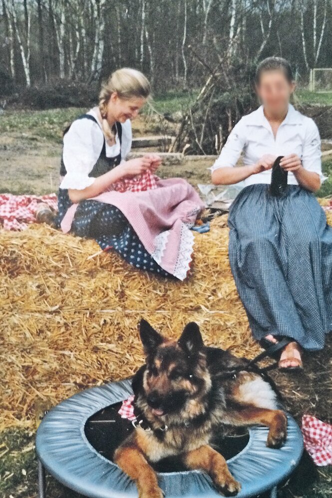 Heidi Benneckenstein sitzt als Jugendliche auf einem Strohballen und näht, vor ihr liegt ein Schäferhund