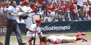 Zwei Baseball-Spieler auf dem Spielfeld, einer liegt auf dem Boden, der andere hockt neben ihm.