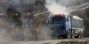 Ein Bulldozer neben einem Lastwagen wirbelt reichlich Staub auf