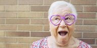 Eine ältere Dame mit einer herzförmigen Brille guckt als hätte sie Spaß