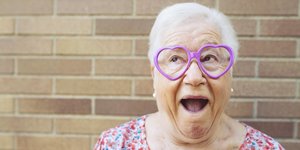 Eine ältere Dame mit einer herzförmigen Brille guckt als hätte sie Spaß