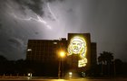 Ein Blitz zuckt den Himmel, daneben ein Hochhaus, an dem eine Lichtinstallation das Konterfei Che Guevaras zeigt