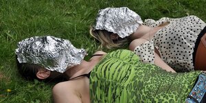 Zwei Frauen liegen auf einer Wiese, sie haben Masken aus Alufolie im Gesicht
