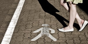 Frauenbeine deuten Schritte an, auf dem Boden ein Piktogramm eines männlichen Fußgängers
