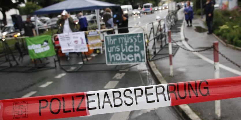 Schild" Ihr müsst uns lieb haben" hinter Polizeiabsperrung