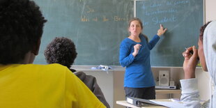 Kinder von hinten, Lehrerin spricht vor einer Tafel