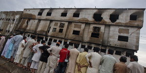 Anwohner stehen vor der abgebrannten Fabrik in Karatschi