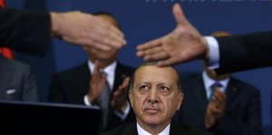 Zwei Leute reichen sich die Hände, Erdogan schaut zu