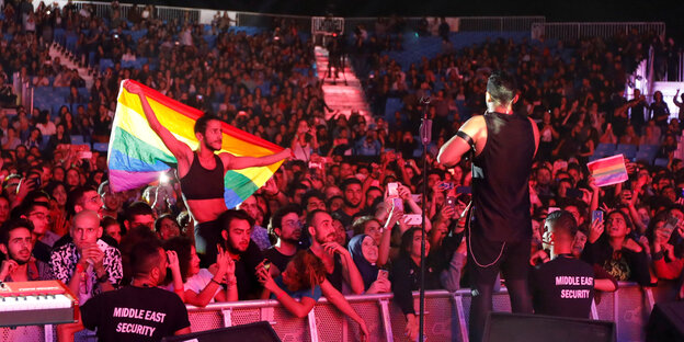 Blick von der Bühne ins Publikum, ein Fan hält eine Regenbogenflagge