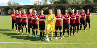 Eine Fußballmannschaft aus Frauen stellt sich pfeilförmig auf.