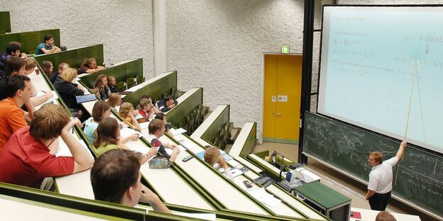 Ein Hörsaal mit Studierenden und ein Dozent an der Tafel vorne.