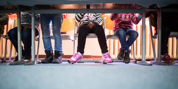 Die Beine von Grundschülern sind unter einem Schultisch zu sehen