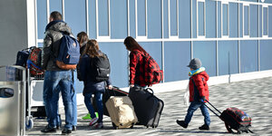 Menschen in dicken Jacken schleifen Koffer hinter sich her während sie ein Gebäude betreten