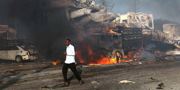 Ein Mann läuft vor Trümmern und einem brennenden LKW vorbei