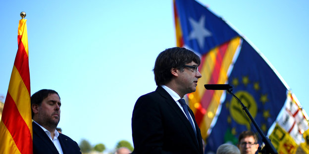 Ein Mann am Mikrofon, im Hintergrund die katalanischen Farben