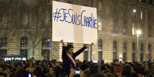 eine Frau hält in einer Menschenmenge ein Schild mit #JeSuisCharlie hoch