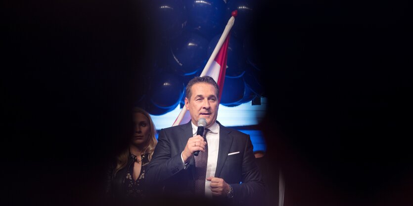 Hein-Christian Strache steht vor einer Flagge Österreichs, um ihn herum ist sonst alles schwarz