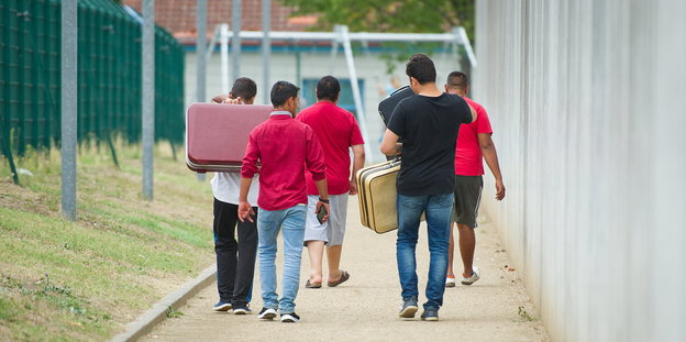 Männliche Flüchtlinge laufen mit Koffern bepackt den Weg zu einer Erstaufnahmeeinrichtung entlang