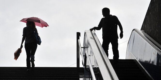 Eine Frau geht die Treppe hoch, ein Mann auf der Rolltreppe dreht sich nach ihr um und schaut ihr hinterher