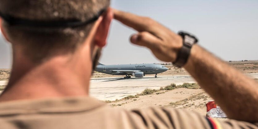 Ein Soldat salutiert, dahintere ein Flugzeug