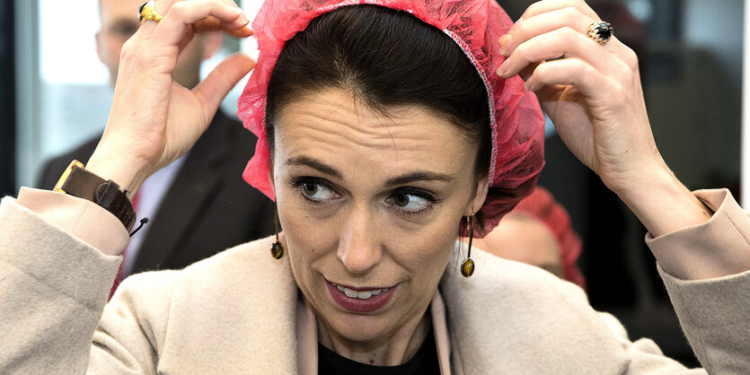 Jacinda Ardern zieht sich eine rosa Haube über den Kopf