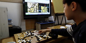 Ein Junge spielt Go vor einem Computer, der ein Go-Spiel anzeigt