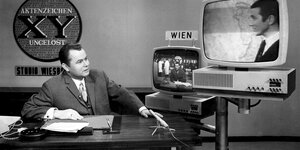 Moderator Eduard Zimmermann an seinem Schreibtisch unterhält sich mit jemandem in einem Fernseher