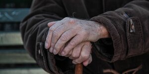 Die Hände eines alten Menschen umgreifen Gehstock