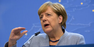 Angela Merkel spricht in ein Mikrofon und hebt die Hand