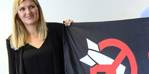 Eine Frau mit einem schwarzen Banner, das ein rotes "Peace"-Zeichen und einen kaputten Atomwaffenkopf zeigt