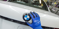 Eine Hand fasst auf ein BMW-Logo in einer Fabrik