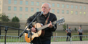 Peter Yarrow steht vor dem Pentagon, spielt Guitarre und singt in ein Mikrofon