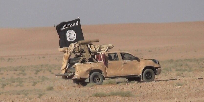 Ein Auto fährt mit sschwarz-weißer Flagge in trockener Landschaft