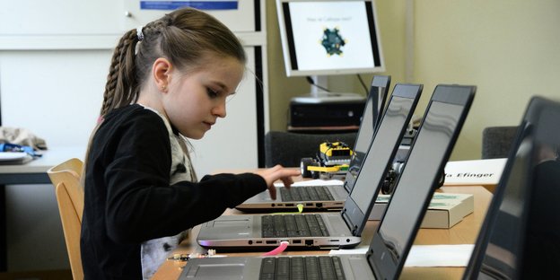Ein Mädchen sitzt vor einer Reihe Laptops und hält die Hand über eine Tastatur