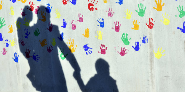 Der Schatten eines Mannes mit zwei Kindern auf einer Wand mit farbigen Handabdrücken