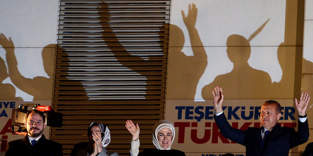 Berat Albayrak, seine Frau und Recep Tayyip Erdogan sowie sein Frau stehen nebeneinander und heben die Arme. Hinter ihnen zeichnen sich ihre Schatten an einer Wand ab