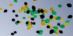 Viele Luftballons in den Farbn schwarz, grün und gelb an einem blauen Himmel