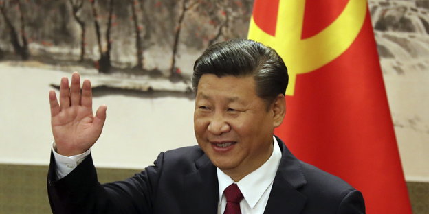ein Mann mit erhobener rechter Hand, im Hintergrund eine chinesische Fahne