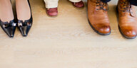 Drei Paar Schuhe sind zu sehen: Frauenlackschuhe, Kinderschuhe, braune Herrentreter