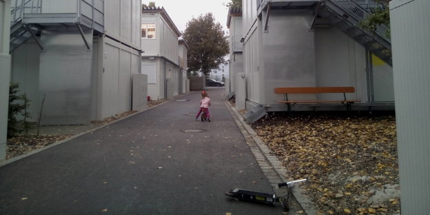 Ein kleines Mädchen fährt mit einem Fahrrad zwischen Containern einen Weg entlang