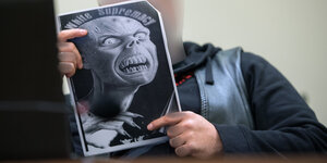 Eine white-Supremacy-Monstermaske ist auf einem Poster abgedruckt, das ein Mann in einem Gerichtssaal in den Händen hält