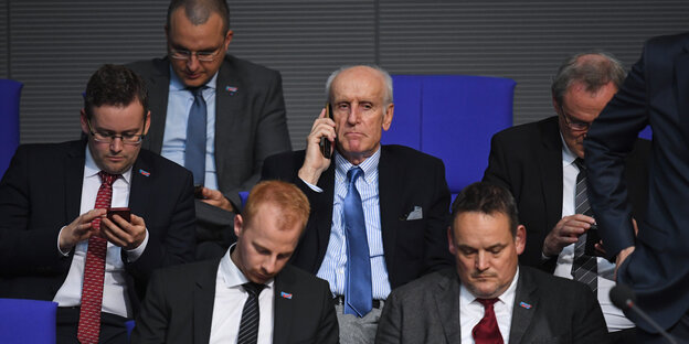 Der 75-jährige AfD-Abgeordnete Albrecht Glaser sitzt mit Telefon am Ohr im Bundestag, umringt von auf Smartphones starrenden, jüngeren Kollegen