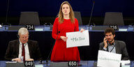 Frau in rotem Kleid hält Schild hoch, auf dem "#MeToo" steht, hinter ihr Stuhlreihen