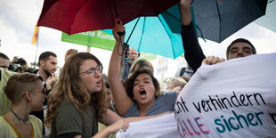 Frauen mit Regenschirmen rufen etwas