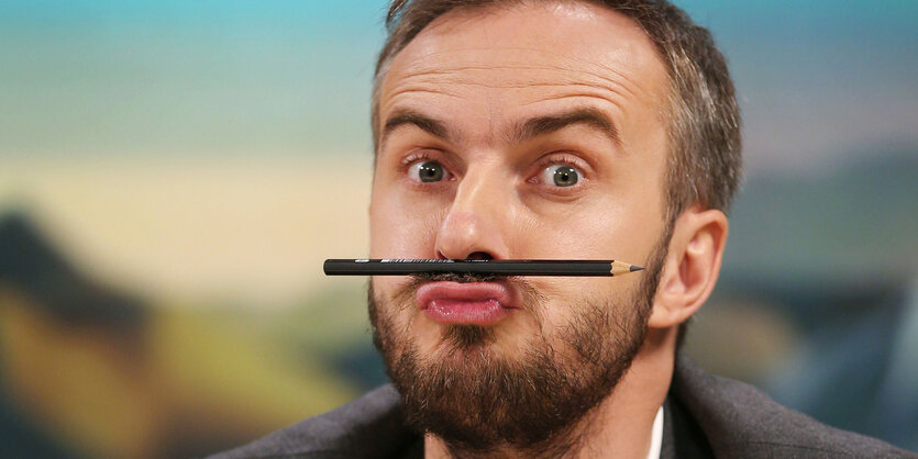 Jan Böhmermann mit einem Stift zwischen Oberlippe und Nase