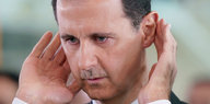 Assad hält sich die Hände hinter die Ohren und guckt betreten