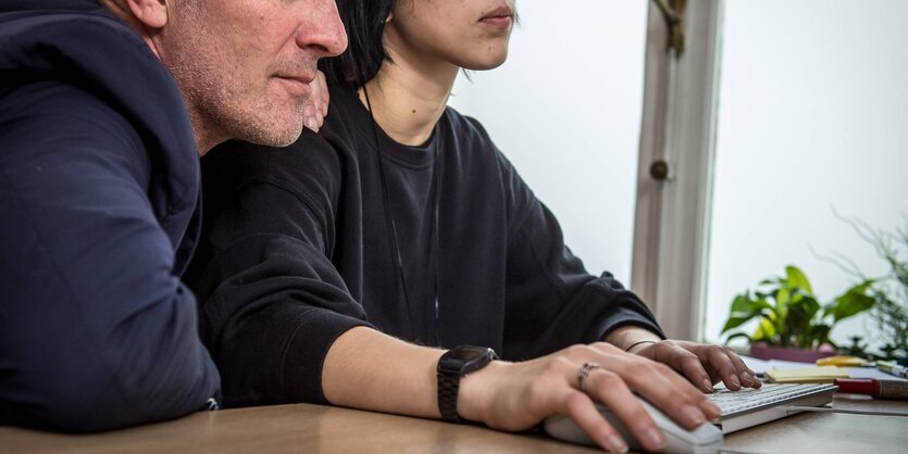 Eine Frau und ein Mann sitzen vor einem Computer. Er fasst ihr an die Schulter