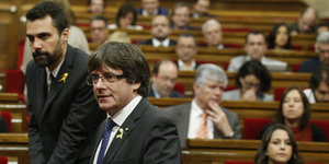 Ein Mann im schwarzen Anzug und mit schwarzen Haaren steht in einem Plenarsaal
