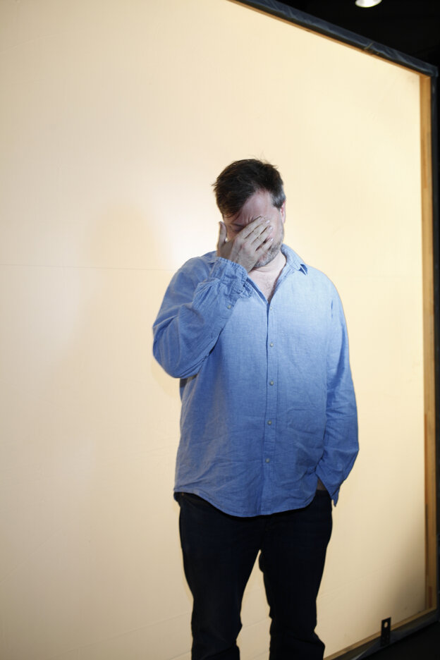 Ein Mann mit blauem Hemd hält sich die Hand vors Gesicht