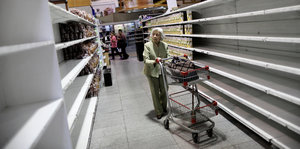 Eine ältere Frau schiebt einen Einkaufswagen durch leere Supermarktregale